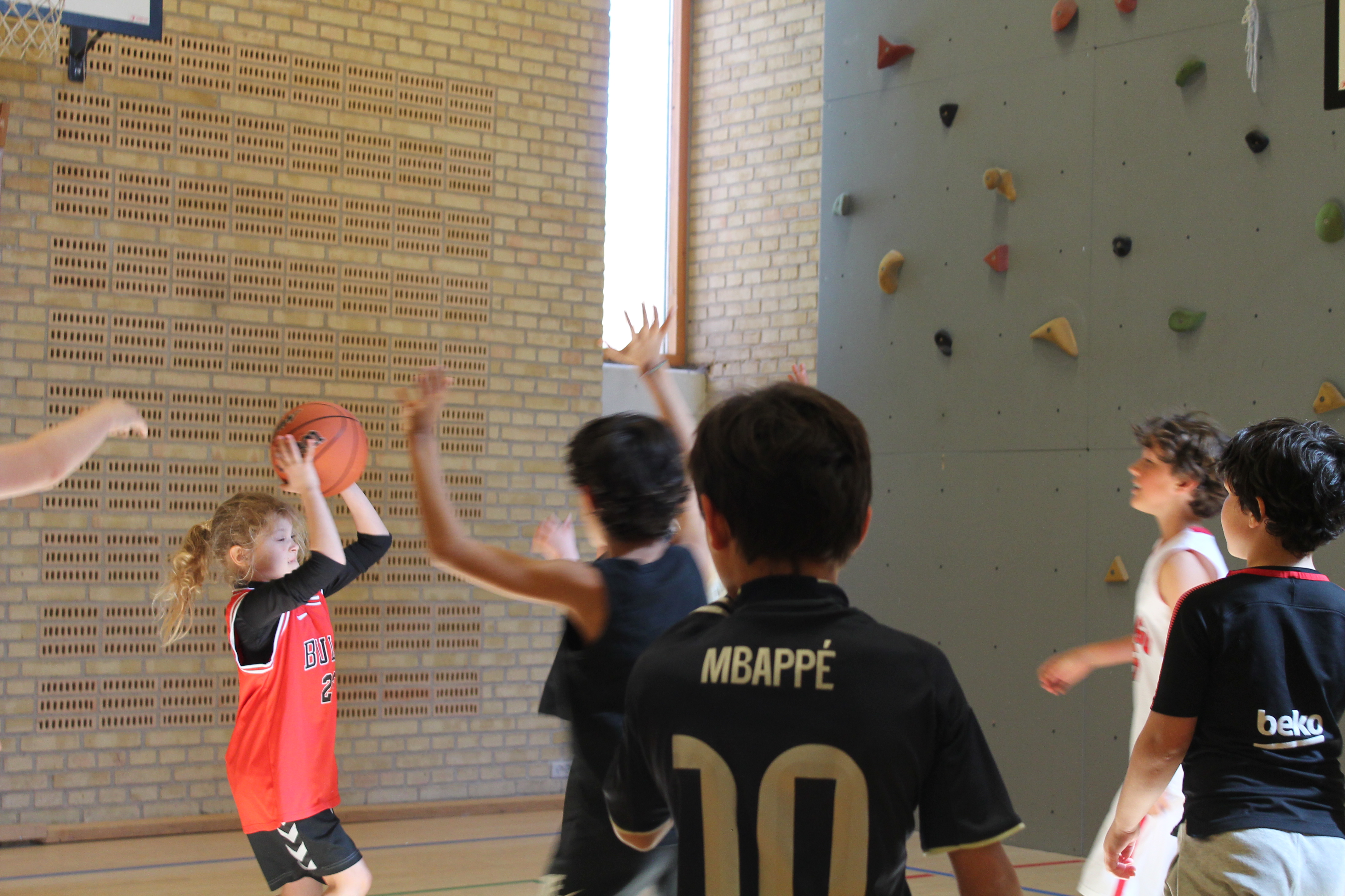 Young player in a Bulls jersey shooting a basketball with the climbing wall behind