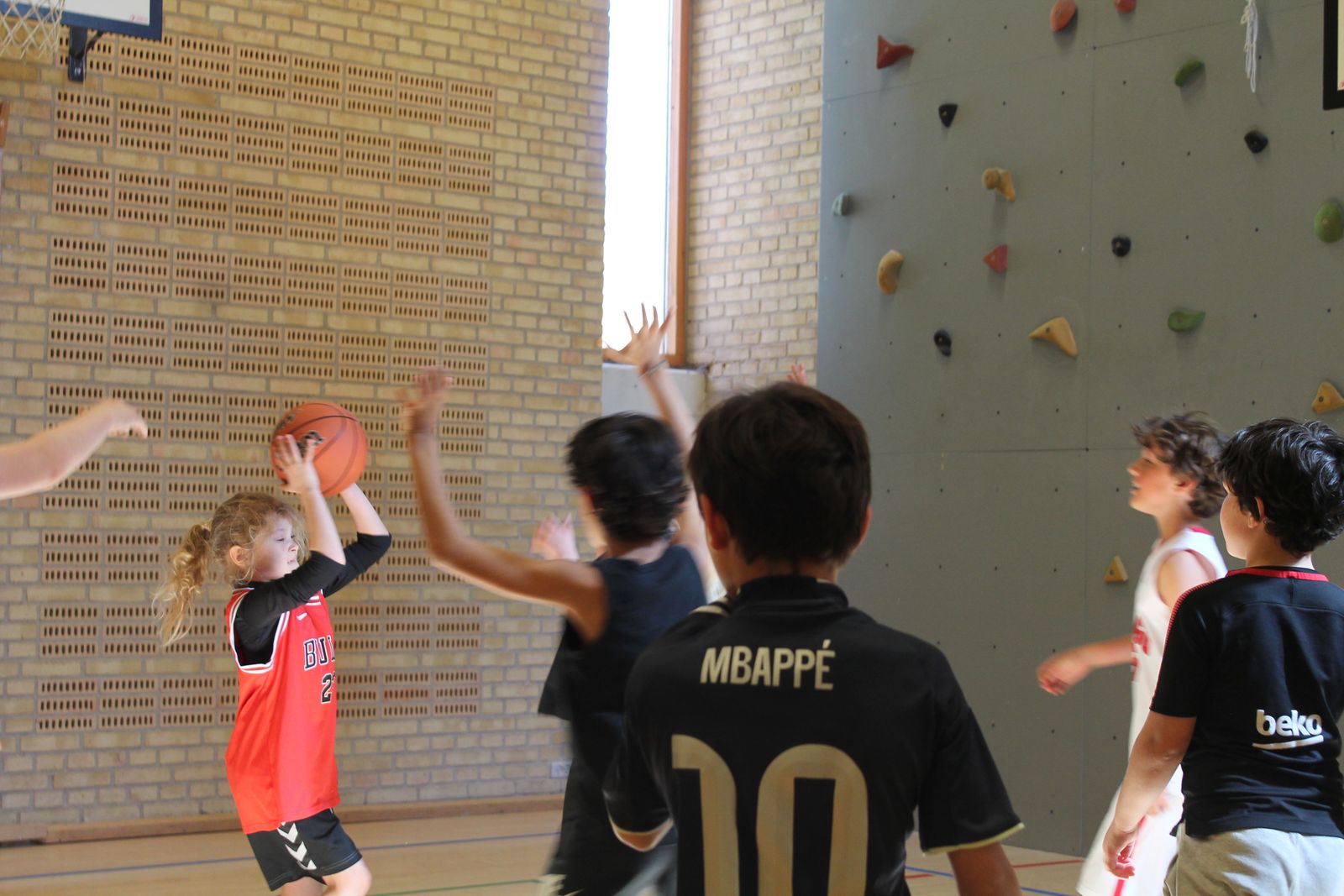 Young player in a Bulls jersey shooting a basketball with the climbing wall behind
